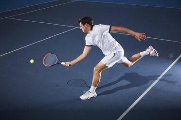 Male tennis player playing tennis, reaching with tennis racket on tennis court - CAIF05817