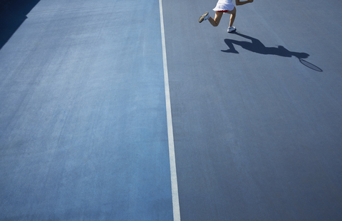 Schatten einer Tennisspielerin, die auf einem sonnigen blauen Tennisplatz läuft, lizenzfreies Stockfoto