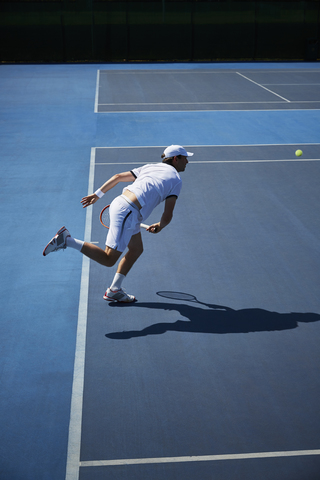 Männlicher Tennisspieler spielt Tennis auf einem sonnigen blauen Tennisplatz, lizenzfreies Stockfoto