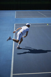Männlicher Tennisspieler spielt Tennis auf einem sonnigen blauen Tennisplatz - CAIF05827