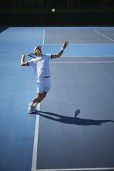 Junger männlicher Tennisspieler, der den Ball auf einem sonnigen blauen Tennisplatz aufschlägt - CAIF05831