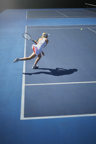 Junge Tennisspielerin spielt Tennis, schwingt den Tennisschläger auf einem sonnigen blauen Tennisplatz, lizenzfreies Stockfoto