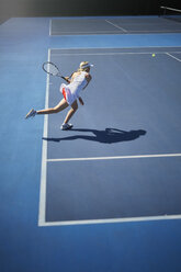 Junge Tennisspielerin spielt Tennis, schwingt den Tennisschläger auf einem sonnigen blauen Tennisplatz - CAIF05835
