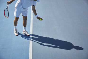 Junger männlicher Tennisspieler, der auf einem sonnigen blauen Tennisplatz einen Tennisball aufprallen lässt - CAIF05836