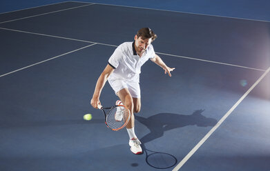 Young male tennis player playing tennis, reaching with tennis racket on blue tennis court - CAIF05839