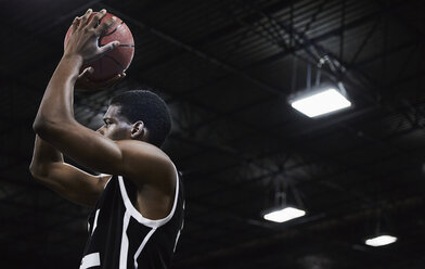 Fokussierter junger männlicher Basketballspieler, der in einer Sporthalle den Ball schießt - CAIF05845