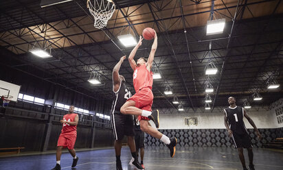 Junge männliche Basketballspieler spielen Basketball auf einem Platz in einer Sporthalle - CAIF05854