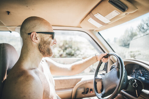 Nackter, fröhlicher junger Mann mit Sonnenbrille und Bart auf einem Road Trip - GUSF00403