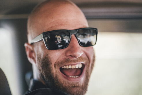 Porträt eines glücklichen jungen Mannes mit Sonnenbrille und Bart auf einer Autoreise - GUSF00415