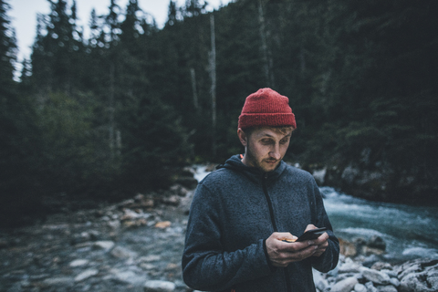 Kanada, British Columbia, Glacier National Park, Mann mit Handy am Illecillewaet River im Wald, lizenzfreies Stockfoto