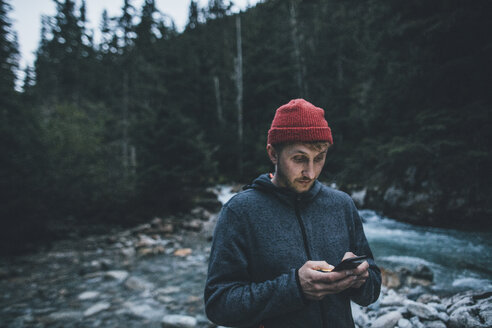 Kanada, British Columbia, Glacier National Park, Mann mit Handy am Illecillewaet River im Wald - GUSF00433