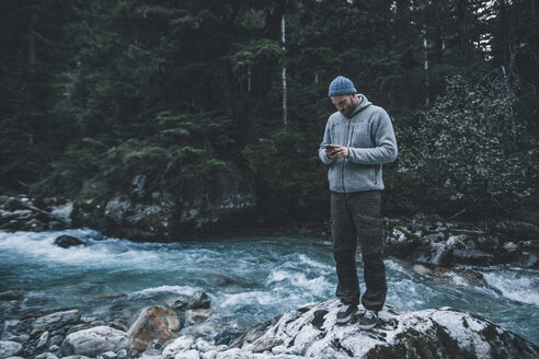 Kanada, British Columbia, Glacier National Park, Mann mit Handy am Illecillewaet River im Wald - GUSF00435