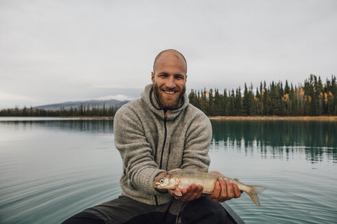 Canada, British Columbia, portrait of smiling man in canoe holding fish on Boya Lake - GUSF00512