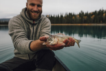 Kanada, British Columbia, Porträt eines lächelnden Mannes in einem Kanu, der einen Fisch auf dem Boya-See hält - GUSF00513
