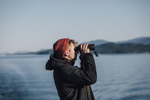 Kanada, British Columbia, Mann schaut durch ein Fernglas auf die Küste - GUSF00523