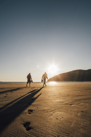 Kanada, British Columbia, Vancouver Island, zwei Männer, die bei Sonnenuntergang am Strand der San Josef Bay spazieren gehen, lizenzfreies Stockfoto