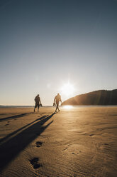 Canada, British Columbia, Vancouver Island, two men walking on beach at San Josef Bay at sunset - GUSF00526