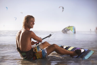 Lächelnder Mann bereit zum Kiteboarding am Strand - CAIF05867