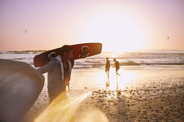 Mann mit Kiteboard am Strand bei Sonnenuntergang - CAIF05869