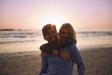 Portrait lächelnd Paar umarmt auf Sonnenuntergang Strand - CAIF05879