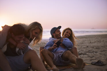 Playful couples hanging out on sunset beach - CAIF05880