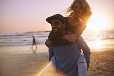 Verspieltes Paar nimmt sich bei Sonnenuntergang am Strand Huckepack - CAIF05891