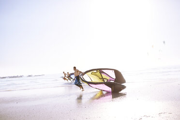 Mann schleppt Kiteboarding-Ausrüstung am Strand - CAIF05893