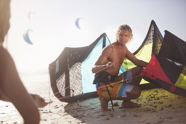 Mann bereitet Kiteboarding-Drachen am sonnigen Strand vor - CAIF05897