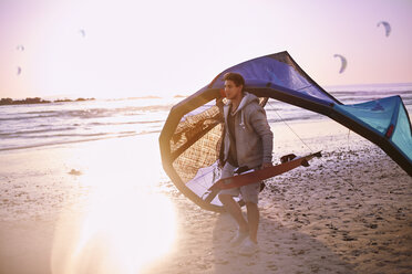 Mann mit Kiteboarding-Ausrüstung am Strand bei Sonnenuntergang - CAIF05900