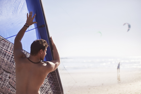 Mann hebt Kiteboarding-Drachen am sonnigen Strand, lizenzfreies Stockfoto