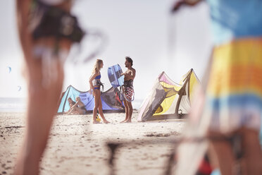 Menschen mit Kiteboarding-Ausrüstung unterhalten sich am sonnigen Strand - CAIF05910