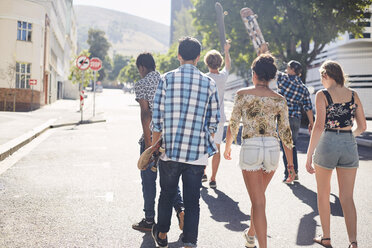 Jugendliche Freunde mit Skateboards zu Fuß auf sonnigen städtischen Straße - CAIF05935