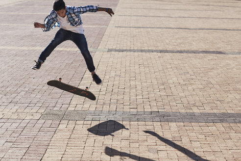 Jugendlicher mit Skateboard auf sonnigem Kopfsteinpflaster - CAIF05936