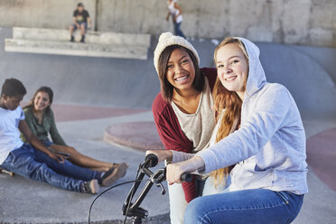 Portrait smiling teenage girls with BMX bicycle at skate park - CAIF05938