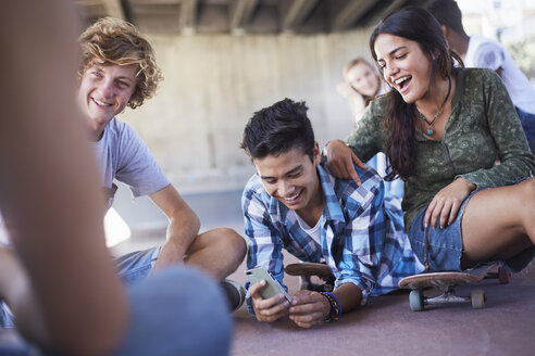 Teenager-Freunde, die im Skatepark mit ihrem Handy SMS schreiben - CAIF05940