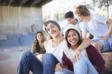 Portrait smiling teenage couple hanging out with friends at skate park - CAIF05949