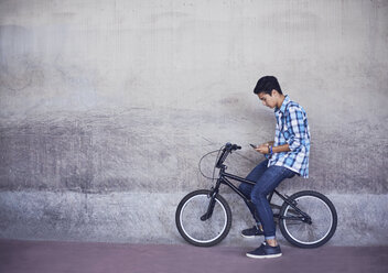 Teenage boy texting on BMX bicycle at wall - CAIF05953