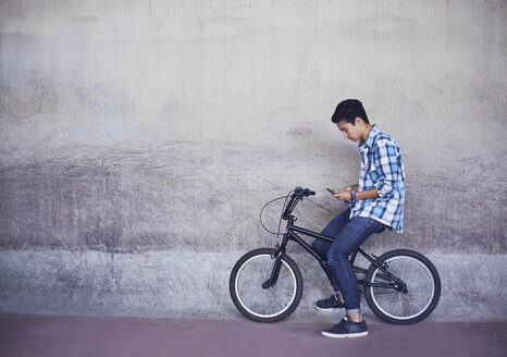 Jugendlicher auf BMX-Rad an der Wand schreibend - CAIF05953