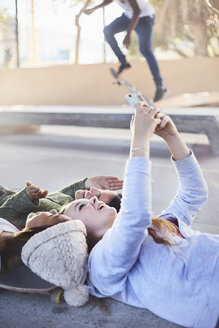Teenager-Mädchen liegen und machen ein Selfie mit einem Fotohandy im Skatepark - CAIF05955