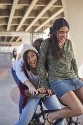 Playful teenage girls riding BMX bicycle at skate park - CAIF05959