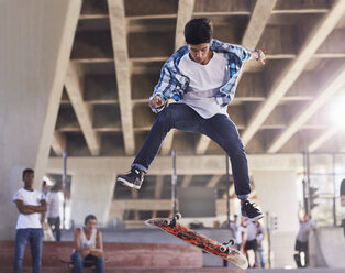 Freunde beobachten einen Teenager, der im Skatepark mit dem Skateboard flippt - CAIF05960