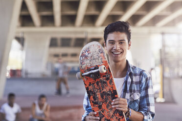 Porträt eines lächelnden Teenagers, der ein Skateboard in einem Skatepark hält - CAIF05968