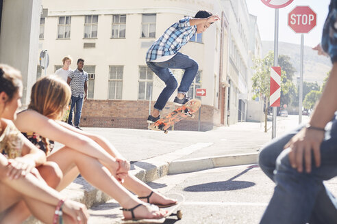 Freunde beobachten einen Teenager, der in einer sonnigen Ecke der Stadt Skateboard fährt - CAIF05971