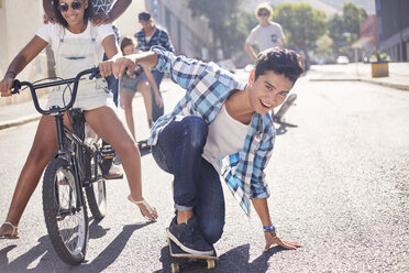 Portrait smiling teenage boy skateboarding with friends on sunny urban street - CAIF05973