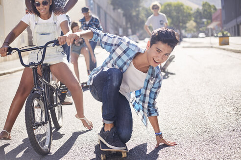 Porträt lächelnd Teenager Junge Skateboarding mit Freunden auf sonnigen städtischen Straße - CAIF05973