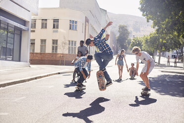 Teenager-Freunde beim Skateboarden auf einer sonnigen Straße - CAIF05974