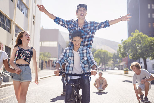 Freunde im Teenageralter fahren BMX-Rad und Skateboard auf einer sonnigen städtischen Straße - CAIF05977