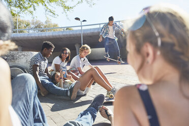 Teenage friends hanging out skateboarding at sunny skate park - CAIF05981