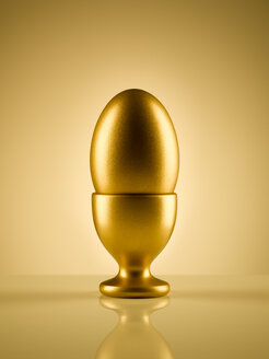 Goldenes Ei im Eierbecherhalter vor goldenem Hintergrund - CAIF05983