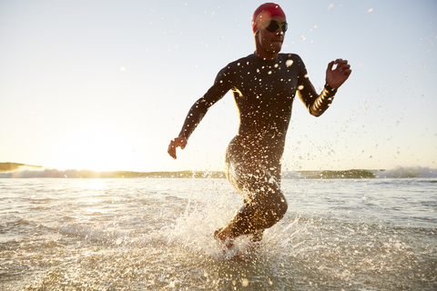 Männlicher Triathlet Schwimmer im Neoprenanzug, der aus dem Meer läuft, lizenzfreies Stockfoto
